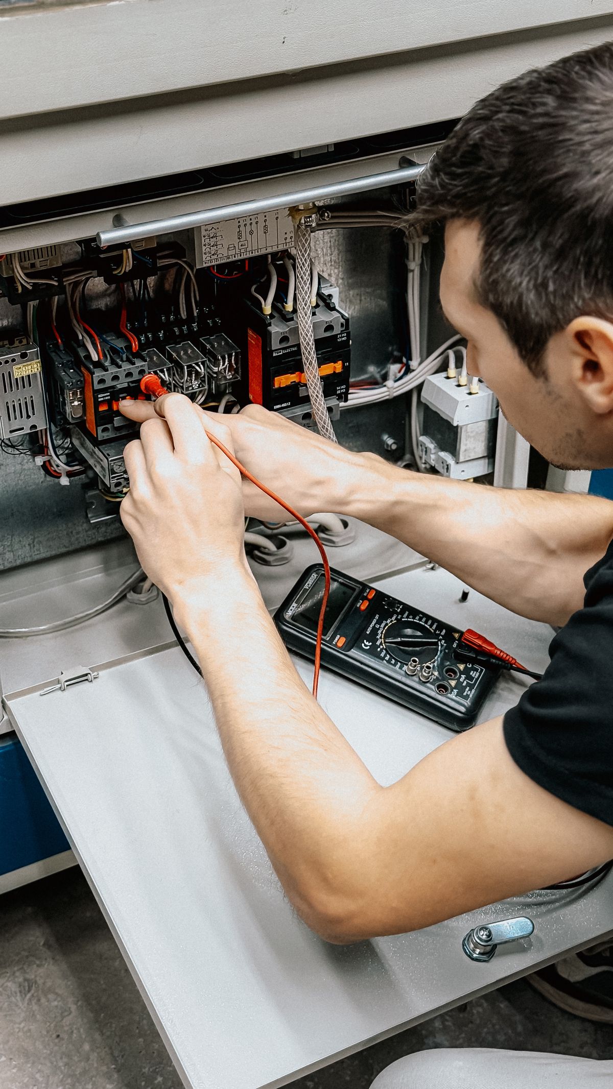 Electrician using a multimeter to test connections inside an electrical panel